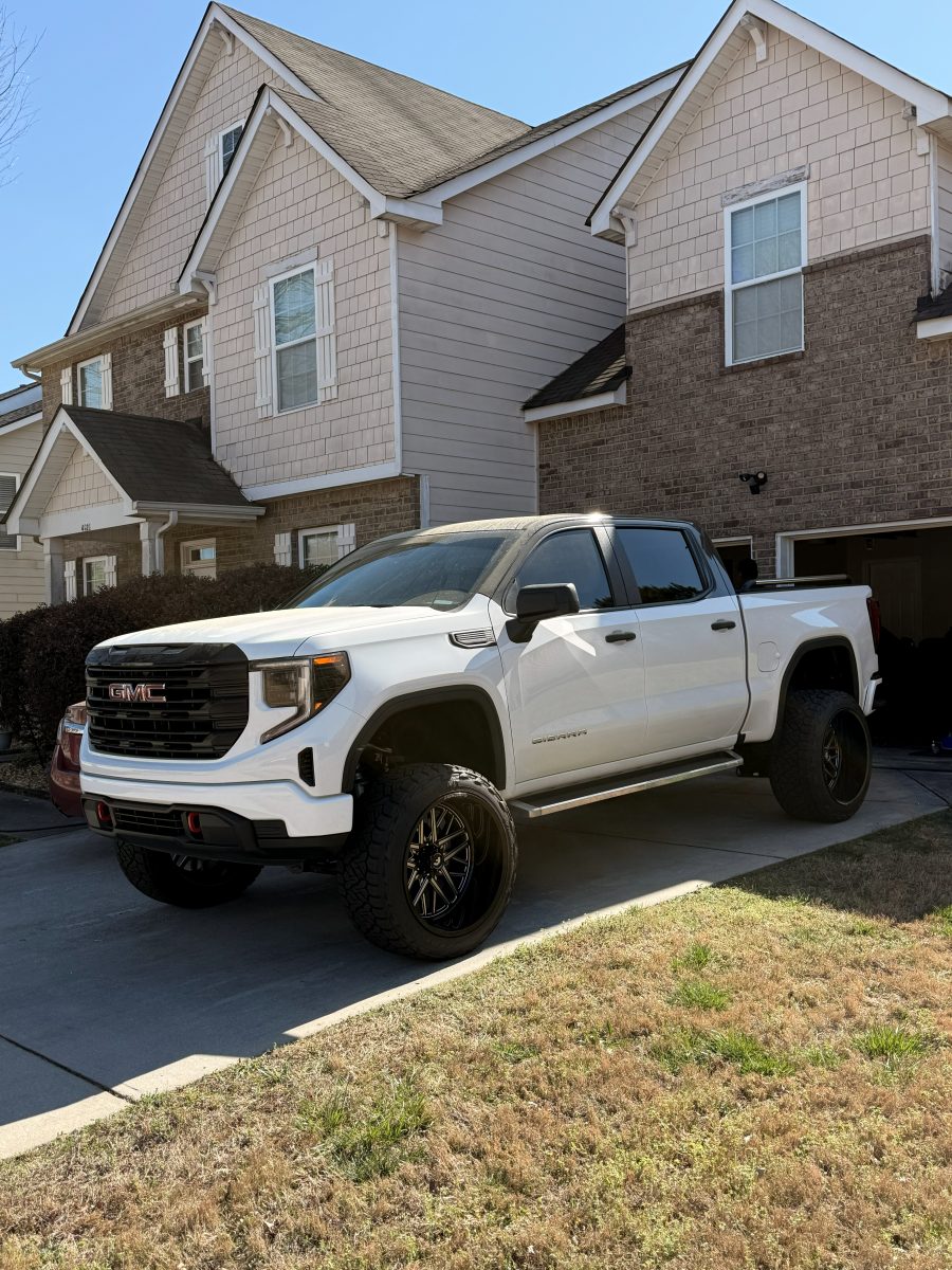 Lifted white GMC Sierra with tinted glass, parked in a driveway